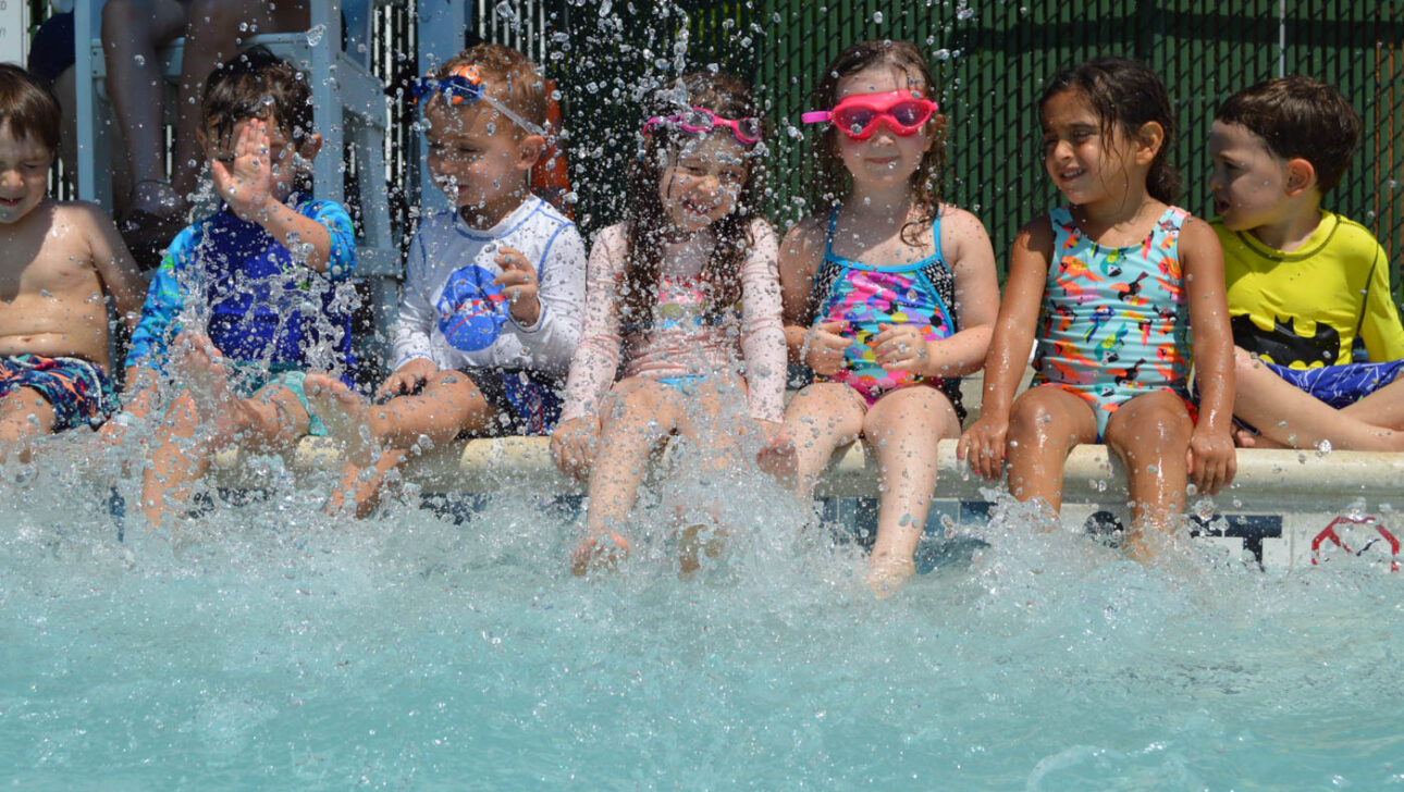 Kids sitting on the edge of the pool splashing the water with their feet.