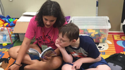 Teen girl reading to a young boy.