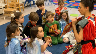 Kids dressed up in costumes listening to the teacher read a book.
