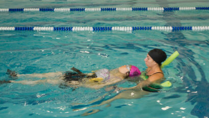 Swim instructor helping a woman swim in the pool.